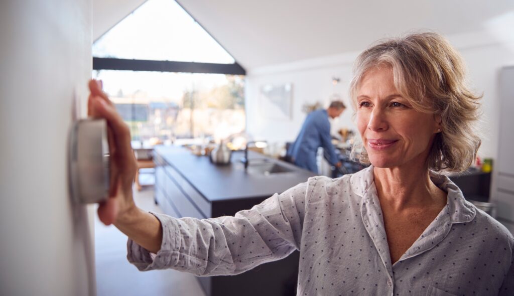 Mature Woman Adjusting Wall Mounted Digital Central Heating Thermostat Control At Home